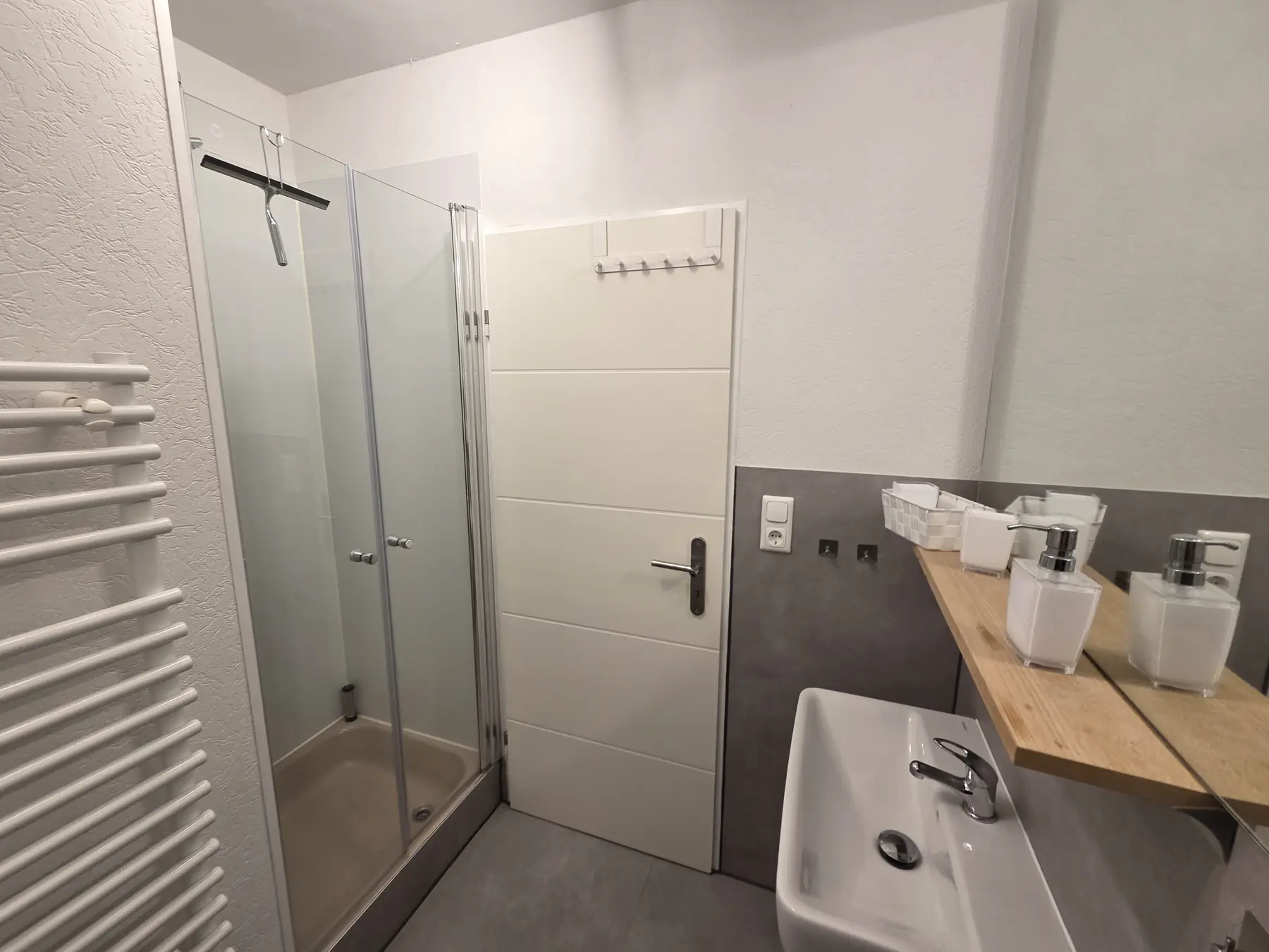 Badezimmer mit Dusche, Waschbecken und Handtuchheizkörper